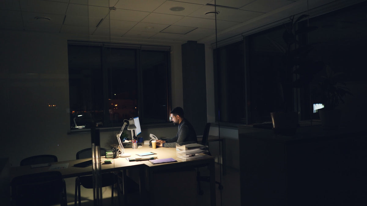 A person working late at a dimly lit office desk under artificial light